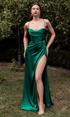 A woman stands outdoors on grass near trees wearing the Ladivine 7483, a long satin prom dress with a corset-style bodice and high slit in emerald green.